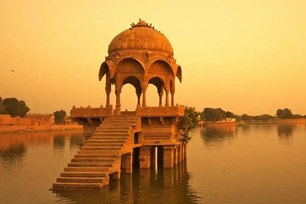 A carved sandstone pavilion reflected in the water at sunset